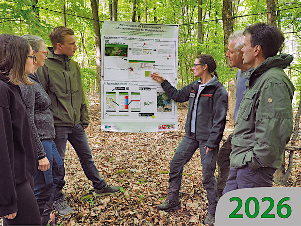 Eine Gruppe Waldbesitzender im Wald steht vor einem Poster und lässt sie von einer Försterin die Baumartenempfehlungen erklären.