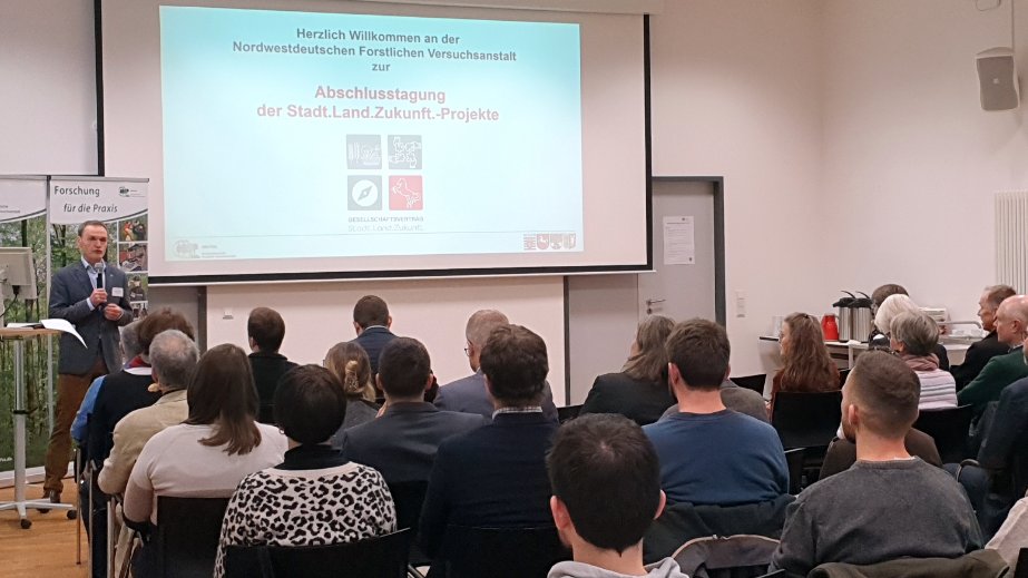 Menschen in einem Saal. Vorne steht ein Redner.